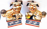 Two hand-painted antique Asian foo dog porcelain figurines sitting on rectangular pedestal bases with floral design.