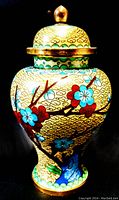 Front and side view of vintage Asian cloisonne ginger jar showing detailed colorful flowers and branches on yellow cloud-patterned background with gold accents and blue birds.