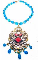 Front view of the vintage brass and lucite rhinestone pendant necklace showing blue faceted lucite beads and ornate brass pendant with rhinestones and coral-red stones with blue drops.