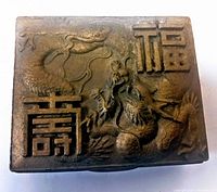 Top view showing metal lid with raised dragon motif and Asian characters, showing details and patina of the metal surface.