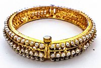 Front-angle view of a vintage gold-tone bangle bracelet decorated with two rows of faux pearls and clear rhinestones, showing the screw clasp with rhinestone detail.