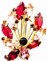 Close-up image showing front of vintage rhinestone brooch with red, pink, amber, and purple marquise-shaped stones set in gold-colored metal.
