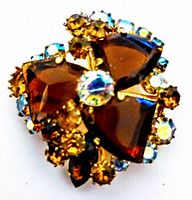 Close-up of brooch showing amber and clear faceted rhinestones set in gold-tone metal with prong settings, floral design.