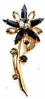 Front view of vintage rhinestone floral brooch showing marquise-cut dark blue and light champagne rhinestones with smaller round rhinestones on gold-tone stem.