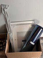 Box containing curtain rod in packaging, two IKEA frames (one visible), and two rolls of dark blue window privacy film.