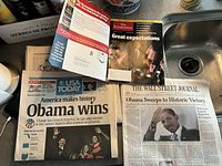 Three newspapers laid out on a surface showing headlines and front pages announcing Obama's 2008 presidential win.