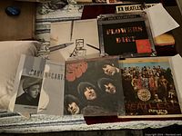 The full lot of vinyl LPs and EPs displayed on a bed. Visible titles include Beatles Rubber Soul remastered, Sgt. Peppers LHCB, Paul McCartney Flowers In The Dirt tour pack (missing vinyl), Pipes of Peace promotional LP, and Once Upon A Long Ago 12" EP.