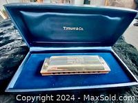 Harmonica resting in dark blue velvet-lined Tiffany & Co. presentation box, lid open showing interior branding.