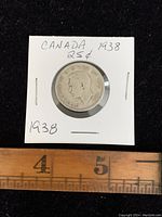 Obverse side of the 1938 Canadian 25 cents silver coin showing King George VI portrait and inscriptions, in a held display with measurement scale below.