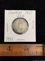 Front side of the 1951 Canadian silver quarter showing King George VI profile in white cardboard holder with handwritten note and a ruler for scale.