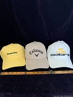 Front view of three golf caps: yellow Pheasant Run, beige Callaway, white Cobra