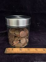 Glass jar about 3.25 inches wide filled with pennies, viewed from front with ruler at bottom for scale.