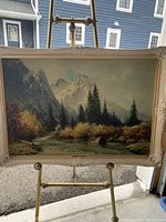 Framed landscape painting on easel, showing the full artwork and frame from an angle.