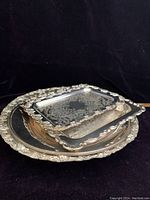 Stacked view of the ornate vintage silverplate trays and footed stand showing embossed floral designs and scalloped edges
