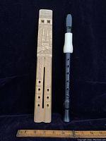 Top-down view of the carved wooden double flute with cathedral engraving alongside black plastic recorder, ruler below for scale
