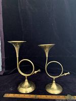 Front view of the two vintage brass horn candle holders side by side on black cloth background, showing their graduated sizes and shiny brass finish.