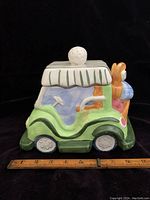 Side view of vintage ceramic golf cart cookie jar showing painted details and lid with golf ball handle, with ruler for scale.
