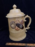 Side view of golden pottery cookie jar featuring raised cookie designs on primary face with ruler at base for scale.