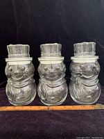 Front view of three identical clear glass snowman candy jars lined up, measuring about 7.75 inches tall each.