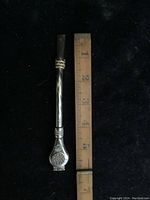 Full length photo of the two-piece silver tone Yerba Mate tea straw displayed with a wooden ruler for scale showing approximately 5 inches in length.