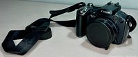 Front view of Canon Powershot S5 IS digital camera with lens cap attached and strap laid out.