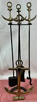 Full view of the vintage brass nautical anchor themed fireplace tools set on a stand showing 3 tools and the stand with brass anchor handles visible.