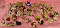 Wide view of approximately 35 assorted small ceramic figurines on a pink fabric surface, showcasing various animals and children figures.