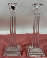 Pair of Waterford Crystal candlesticks standing side by side on a red surface showing their height and stepped square bases.