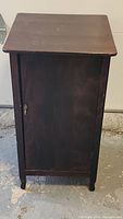 Front view of the antique wooden record cabinet closed, showing the door with metal key lock and four legs.