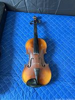 Top-down view of the antique violin without strings attached showing overall front condition, wear, and fingerboard.