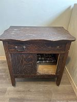 Front view of antique dark brown wooden washstand showing drawer and missing door, highlighting wood grain and scalloped top edge.