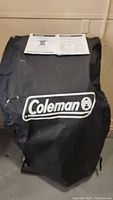 Coleman grill cover with Coleman logo, assembly manual and safe use & care manual on top