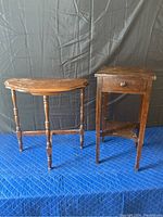 Front view of dark brown solid wood D table and nightstand on blue padded surface with black draped background.