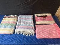 Lot overview showing all four blankets on a blue quilted surface, including the packaged Texmade blanket and three knitted blankets