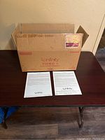 Original brown cardboard box labeled Infinity Video 1 center channel loudspeaker with included paperwork on table.