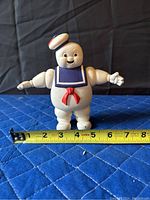 Front view of the Michelin Man figurine with a measuring tape indicating approximately 6 inches tall, placed on a blue quilted surface.
