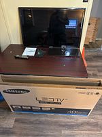 Full view of Samsung LED TV on table with remote, manual, and glass stand, with the original box below the table