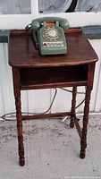 Full view of wooden telephone table with green rotary dial telephone on top.