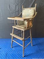 Full view of vintage wooden doll high chair showing attached floral cushion, turned spindle legs, worn wood, and tray with raised edges.