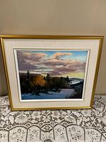 Framed Mont Cascade landscape painting on a lace-covered table against a wall.