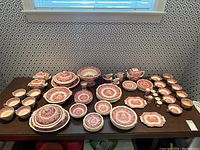 Full display of red and white transferware pieces laid out on table against patterned wallpaper