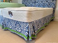 Side view of mattress with blue and white patterned bed skirt featuring green trim