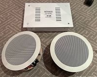 Pair of white round Boston Acoustics DSi455 in-ceiling speakers along with a white Knoll WIN600 stereo interface placed on carpeted floor, showing entire set.