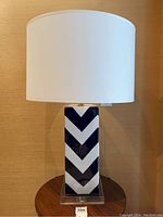 Full view of the blue and white chevron pattern lamp on lucite base with white drum shade on a wooden table