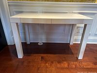 Front view of the white gloss IKEA desk showing the drawer fronts and square legs.