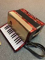 Red Rigolette IV accordion with white and black piano keys visible, along with shoulder straps.