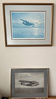 Two framed airplane pictures hung on a white wall, top one in gold-tone frame, bottom one in silver frame.