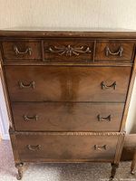 Front view of the antique wooden dresser showing four drawers with decorative handles and a carved floral piece on the top middle drawer.