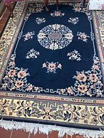 Top-down photo showing entire area rug with central medallion and floral motifs, blue base with cream border, and fringed edges.