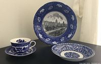 Blue and white porcelain tea cup and saucer alongside two blue and white bowls, one with scenic image of Manchester Royal Infirmary.